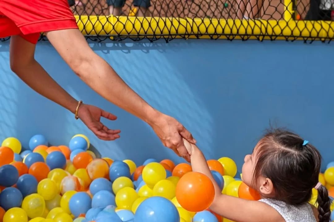 A therapist reaching down to take a child’s hand in the ball pit